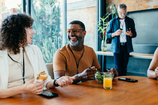 Colleagues enjoying a casual lunch break while sharing laughter and eating healthy food - Powered by Adobe