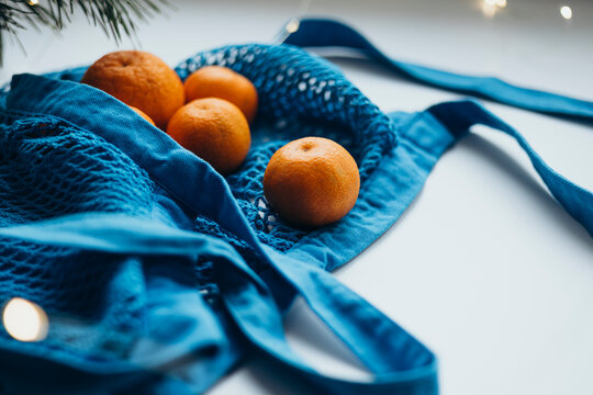 Fresh tangerines in a blue string bag on a light background