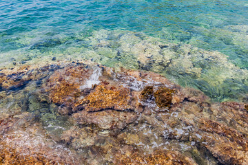 Crystal clear shallow waters revealing colorful rocks and textures beneath the surface in a calm...