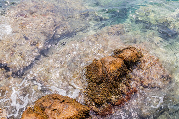 Crystal clear shallow waters revealing colorful rocks and textures beneath the surface in a calm...