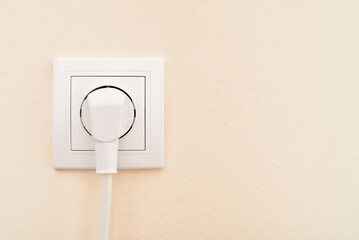 White electric cable plugged in the white power socket on the pale orange wall. Single power socket...