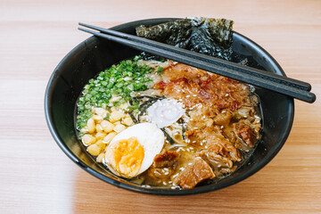 Japanese Ramen with corn, leeks, half of an egg, beef, nori, and narutomaki. Chopsticks on the black bowl. Japanese traditional meal.