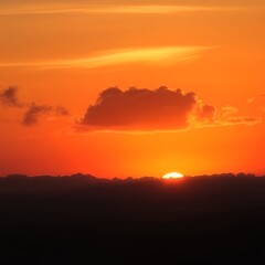 Fototapeta premium A vibrant sunset paints the sky with fiery orange and red hues. Silhouetted mountains create a dramatic backdrop. Peaceful and serene.
