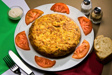 Tortilla española servida con rodajas de tomate en plato blanco.