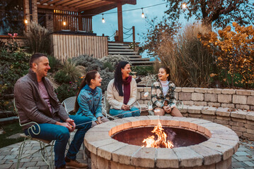Family roasting marshmallows over open flame, campfire on backyard.