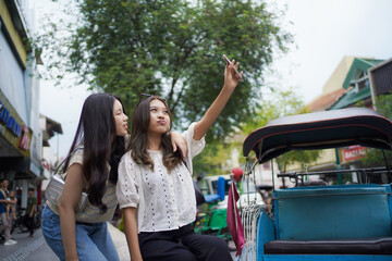 two happy asian women take selfie photos with smart phone on the street