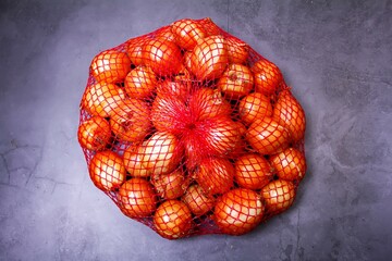a lot of ripe onions in a red mesh on a gray background