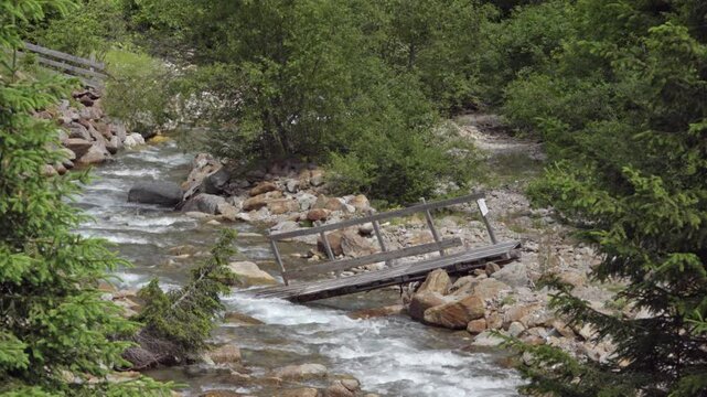 Part of a broken bridge made of pallets and wood lies in a stream bed