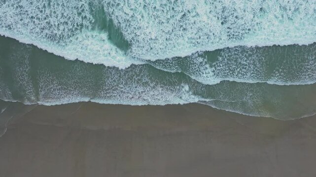 Aerial View Of Foamy Sea Water Splashing On Sandy Beach At Playa de Caion In A Coru&ntilde;a, Spain. top-down, slow-motion shot