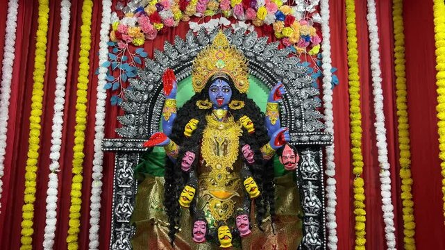 Maa Kali idol in a pandal with a red cloth background and yellow and white flower garlands.