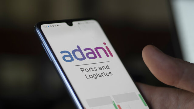 An investor analyzing the adani ports & sez etf fund on a screen. A phone shows the prices of Adani Ports & SEZ