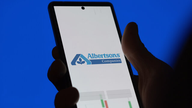 An investor analyzing the albertsons etf fund on a screen. A phone shows the prices of Albertsons