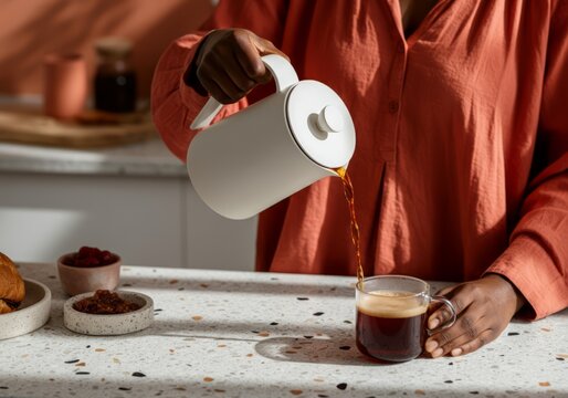 Black woman pouring fresh coffee into a mug in a modern kitchen setting