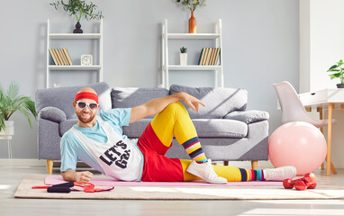 Funny extravagant young man in colored sports clothes lying on the yoga mat surrounded by sports...