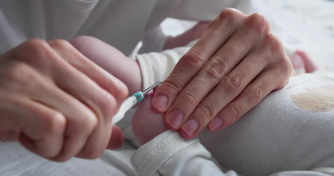 Mother gently clips her baby nails with baby scissors to prevent scratches