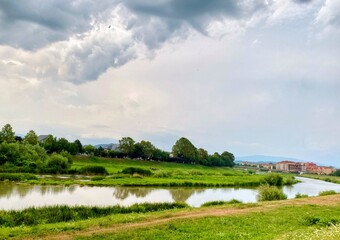 A pictureskue view of a calm river among greenery in the suburbs under a cloudy sky before the rain
