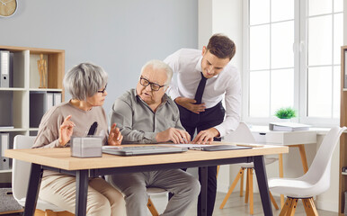 Obraz premium Confident gray-haired elderly senior couple sitting at the desk in office with a young man advisor or male financial agent signing a contract about health insurance or investments.