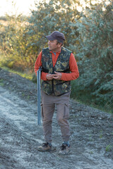Mature hunter man holding a shotgun and walking through a field