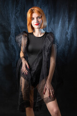 A young red-haired girl in a black bodysuit poses in the studio against a dark background.