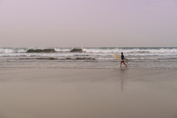 Surfer with surfboard in hands going through beautiful sand beach in Lanzarote, Canary Islands