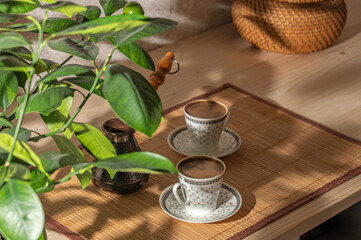 Two cups of coffee and cezve on the table in the patio lit by morning sun.