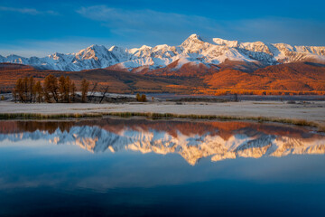 Autumn scenery in Altai with colorful forest, snowy peaks, and perfect water reflections