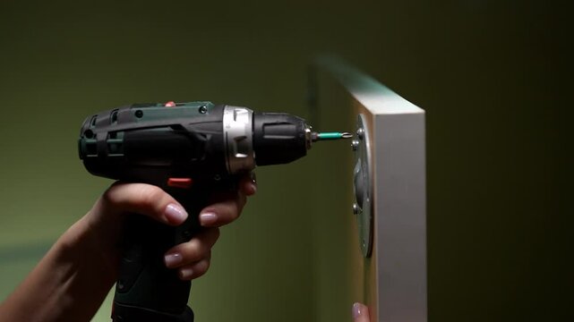 Young woman demonstrating home improvement by using electric drill. Close-up female hands using cordless screwdriver to assemble furniture, showcasing process of home improvement and diy projects.