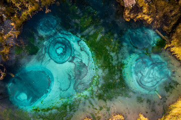 Aerial image showing vivid turquoise geysers in mineral-rich water surrounded by scenic natural...