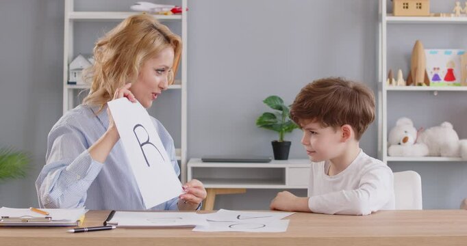 Professional language pathologist working with little kid. Woman therapist doing articulation exercises with happy child boy teaching him to pronounce English R sound correctly. Speech therapy concept