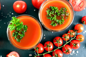 Two glasses with tomato juice stand on a black background.	