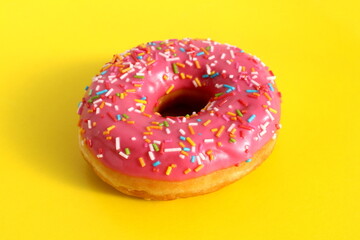 On a yellow background lies a sweet donut with pink icing and sugar sprinkles.