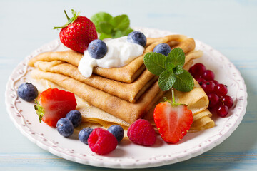 Crepes, thin pancake stack with yogurt and berries. Wrapped pancakes on a plate