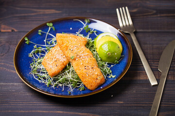 Fried salmon steak with microgreens, lemon and lime on blue plate