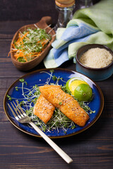 Fried salmon steak with microgreens, lemon and lime on blue plate
