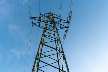 Sunlit high voltage pylon with overhead power lines und a blue summer sky with some small white clouds. Horizontal photograph.