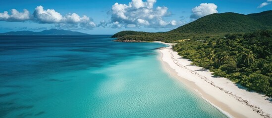 Aerial view of a pristine white sand beach meeting vibrant turquoise waters near lush green mountains under a clear blue sky.