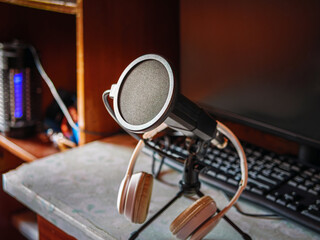 Podcast microphone resting on a desk in a recording ready podcasting home studio. Selective focus of podcast equipment in empty room, ready to be used for online streaming