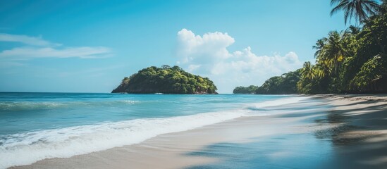 Fototapeta premium Tranquil beach scene featuring soft sand and a lush green island surrounded by clear ocean waters under a bright blue sky