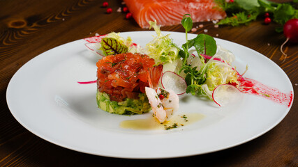 Avocado Salmon Tartar. Seafood appetizer. Avocado salmon tartar starter plate served with fresh vegetable salad.