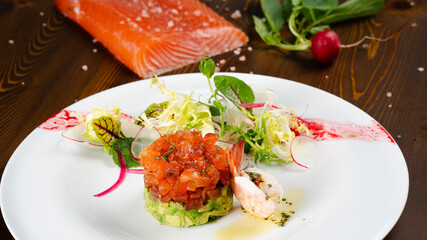 Avocado Salmon Tartar. Seafood appetizer. Avocado salmon tartar starter plate served with fresh vegetable salad.