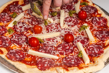 The chef's hands spread the ingredients on the pepperoni pizza. Pizza on a baking wheel, ready to be sent to the oven. in