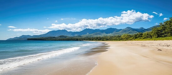 Obraz premium Scenic sandy beach with mountain backdrop under blue sky showcasing tranquility and natural beauty in a coastal landscape