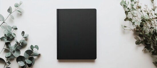 Elegant black notebook mockup surrounded by greenery on a minimalist white background perfect for text placement and creative design presentations