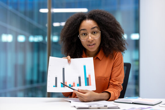A professional woman explains data trends using graphs during a business meeting in a modern office. Her presentation focuses on statistical analysis while fostering teamwork and professional growth