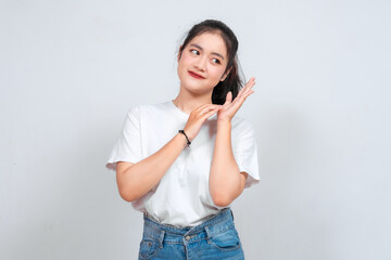 A young Asian woman stands against a white background, smiling warmly with her hands together in front, expressing happiness and contentment.