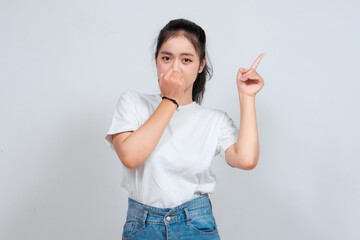 Scared Asian woman looking to the copy space upwards while covering her mouth. She is in a state of...