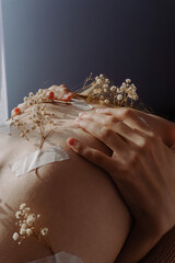 An artistic display of dried flowers and hands delicately placed on a human back, evoking themes of...