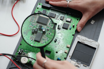 Examining Electronic Circuit Board with Magnifying Glass