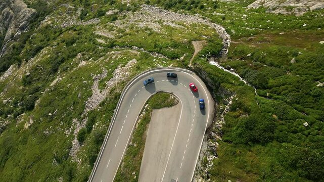 Aerial overhead drone view of cars driving round hairpin bend in road.
