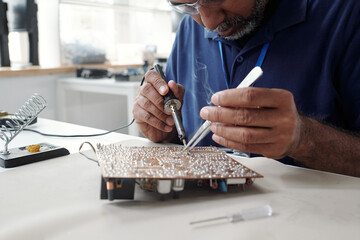 Man Soldering Circuit Board in Electronics Workshop